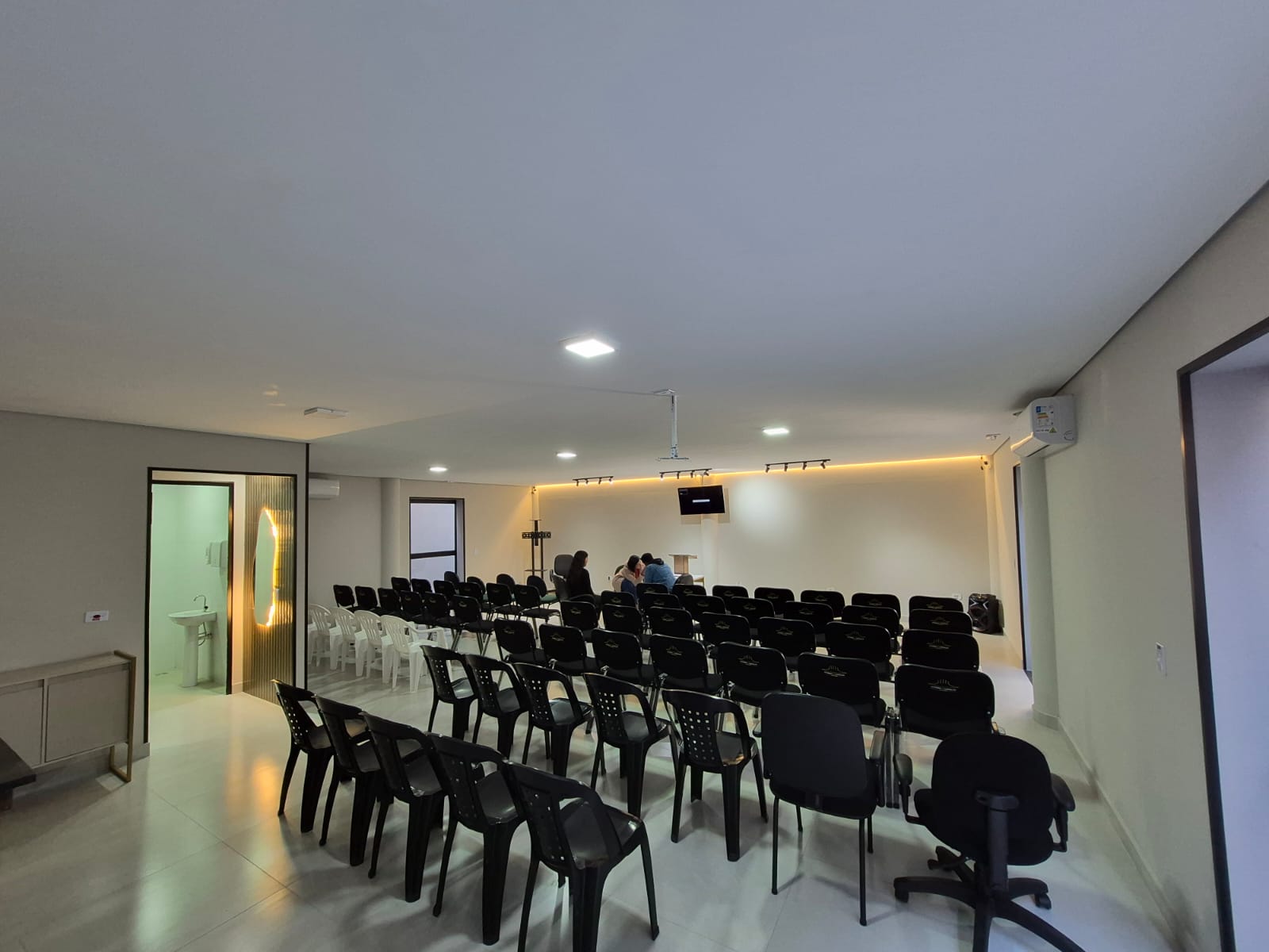 Salão do auditório visto do fundo, com fileiras de cadeiras pretas e iluminação de teto.